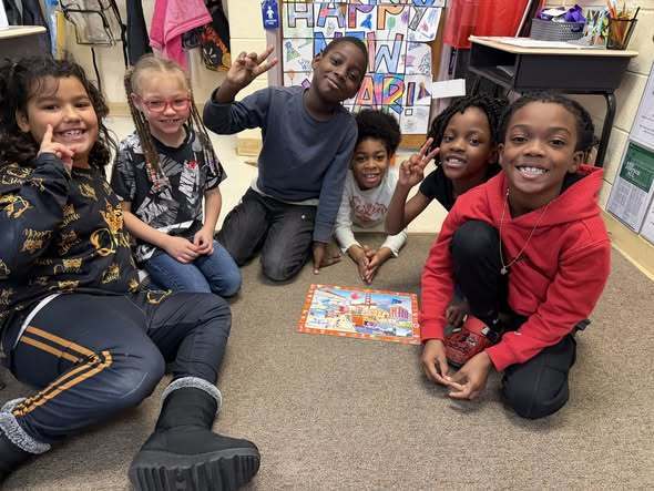 Kids sitting in a classroom smiling while putting together a puzzle. 