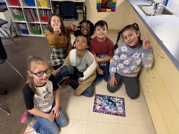 Kids sitting on the floor and smiling in a classroom. 