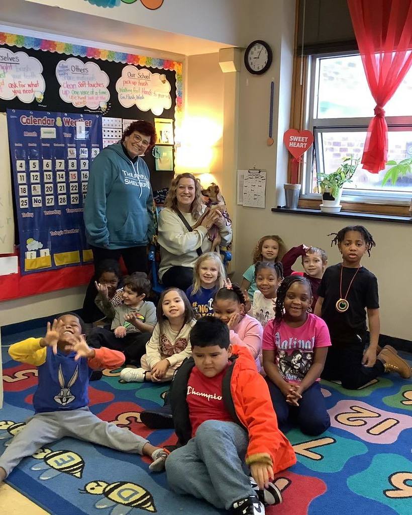 A group photo of kids, adults and a dog  in a classroom 