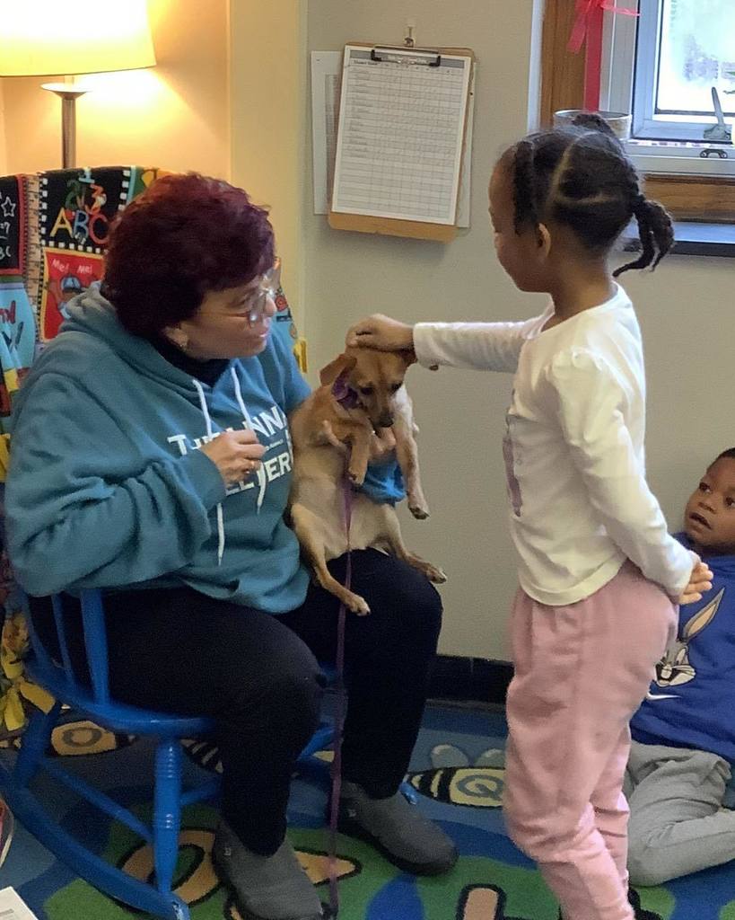 Child petting a small dog that a women in a blue hoodie is holding. 