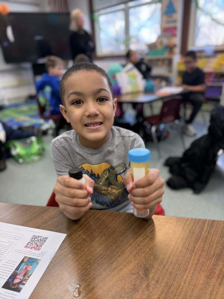 Young boy in a pgray shirt smiling and holding two tubes. 
