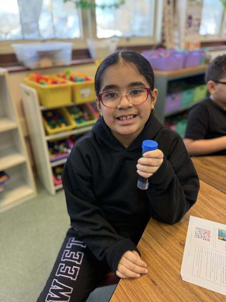 Young girl in a black hoodie smiling and holding a tube of blue liquid. 
