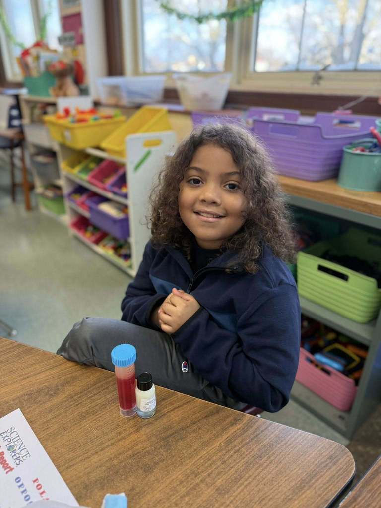 Young girl in a navy blue shirt smiling in a classroom. 