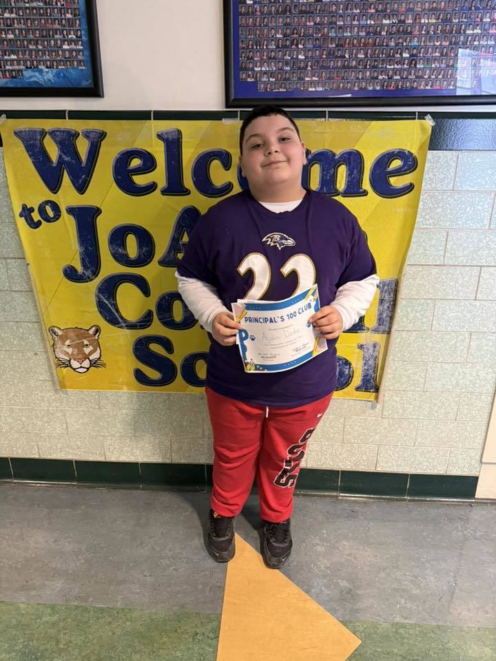 Young boy in red pants holding his certificate.