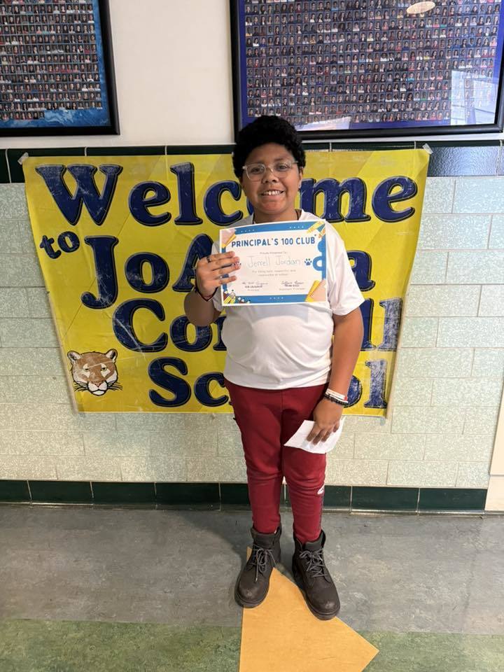 Young boy in red pants holding his certificate.