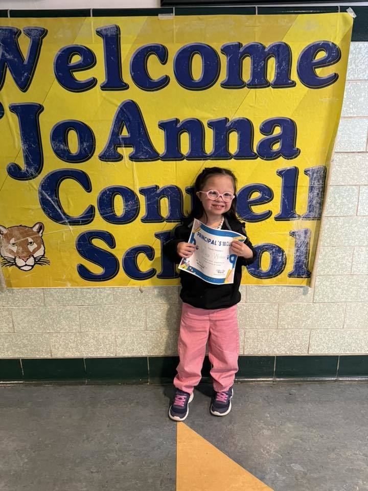 Young girl in pink pants and glasses holding her certificate.