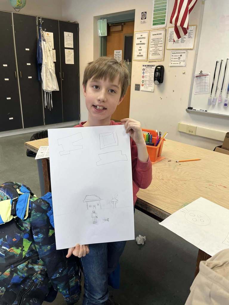 Young boy holding up her drawing.
