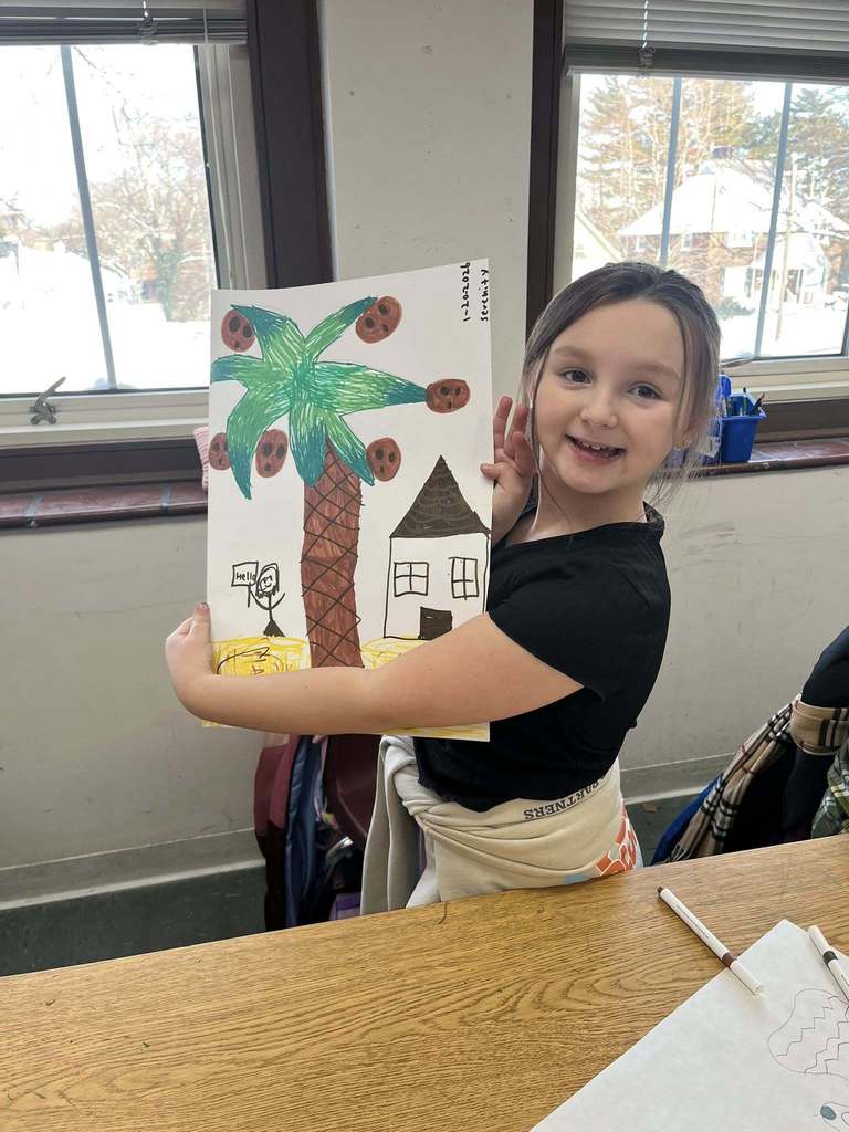 Young girl in a black shirt holding up her drawing.