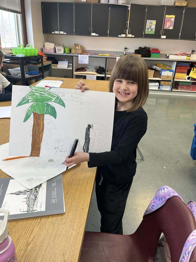 Young girl in a black shirt holding up her drawing.