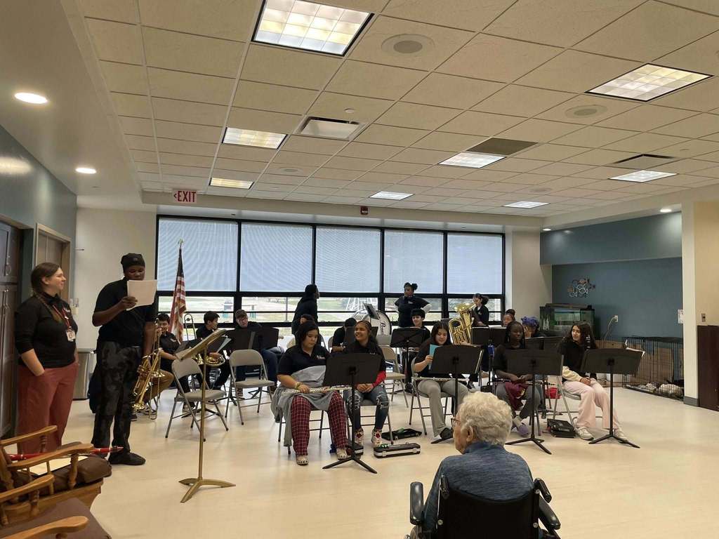 Kids sitting and preparing to play their instruments, while a n elderly lady in a wheel chair sits in front and watched. 