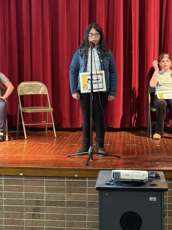 Young girl standing at a microphone on a stage.