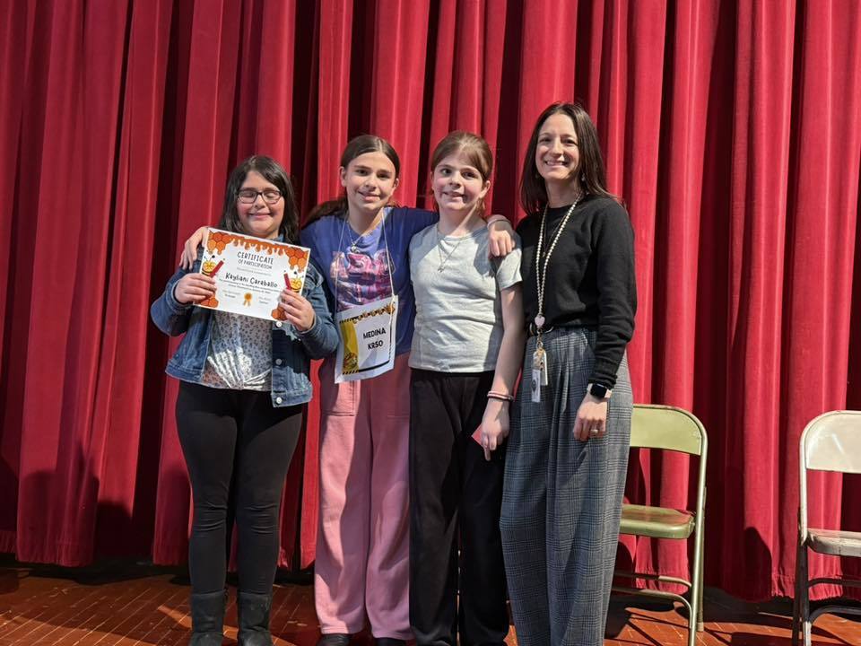 Kids and adulton stage standing against a red curtain.