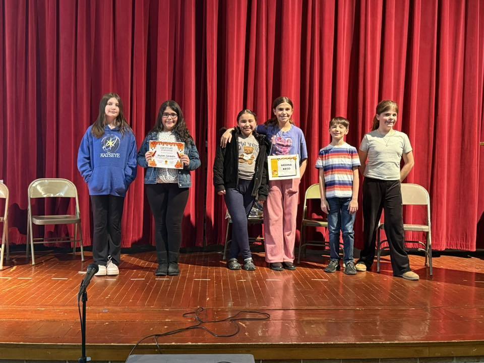 Kids on stage standing against a red curtain.