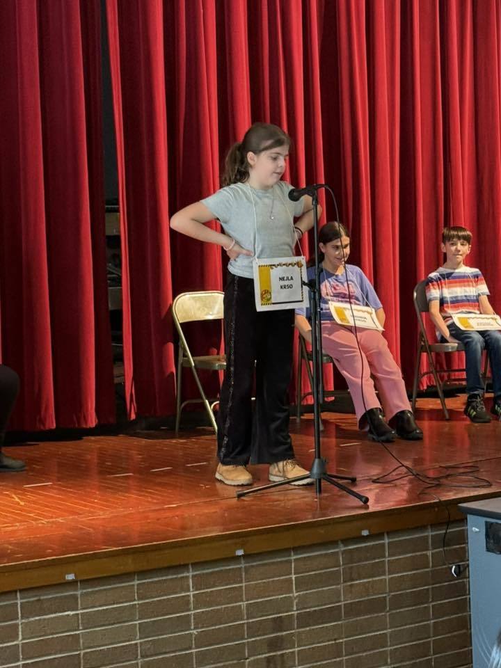 Young girl standing at a microphone on a stage.