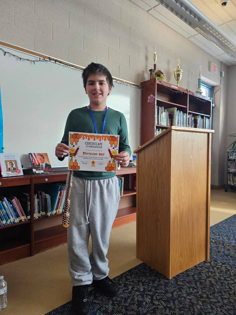 Young boy in a green shirt holding his certificate.