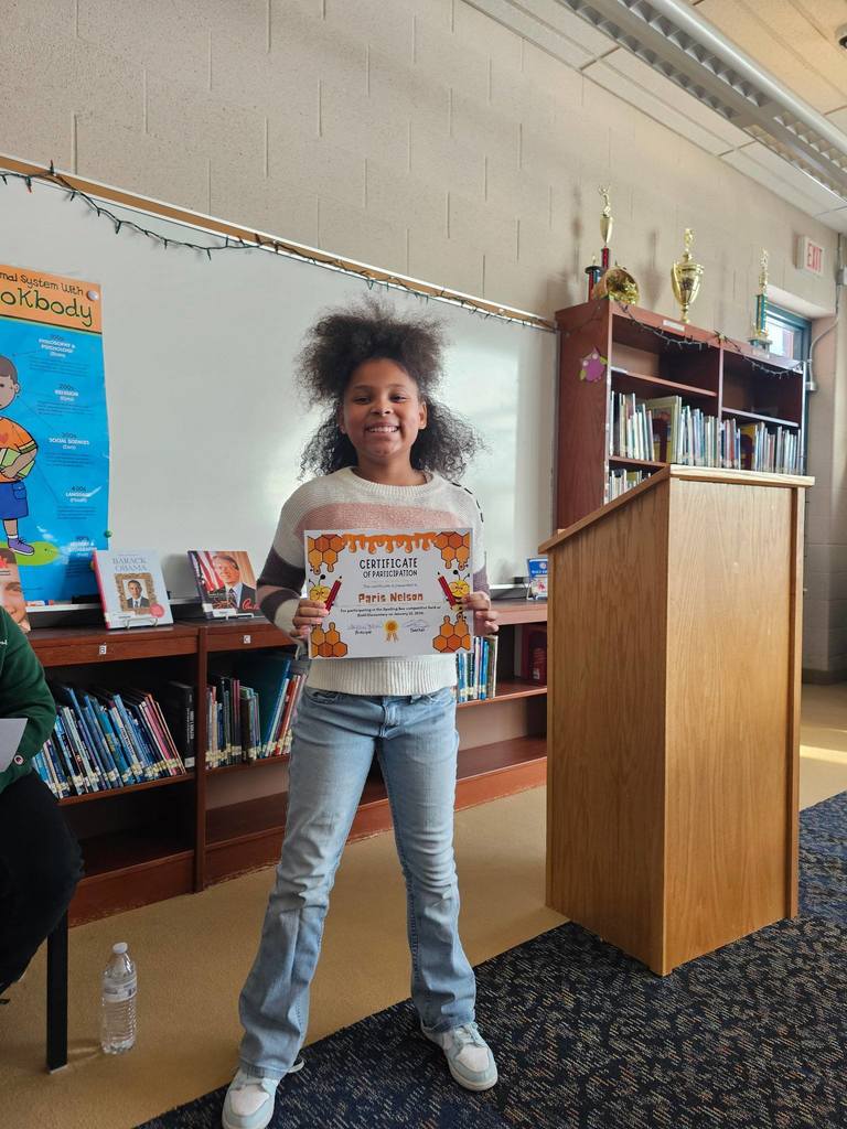 Young girl in a classroom holding her certificate.