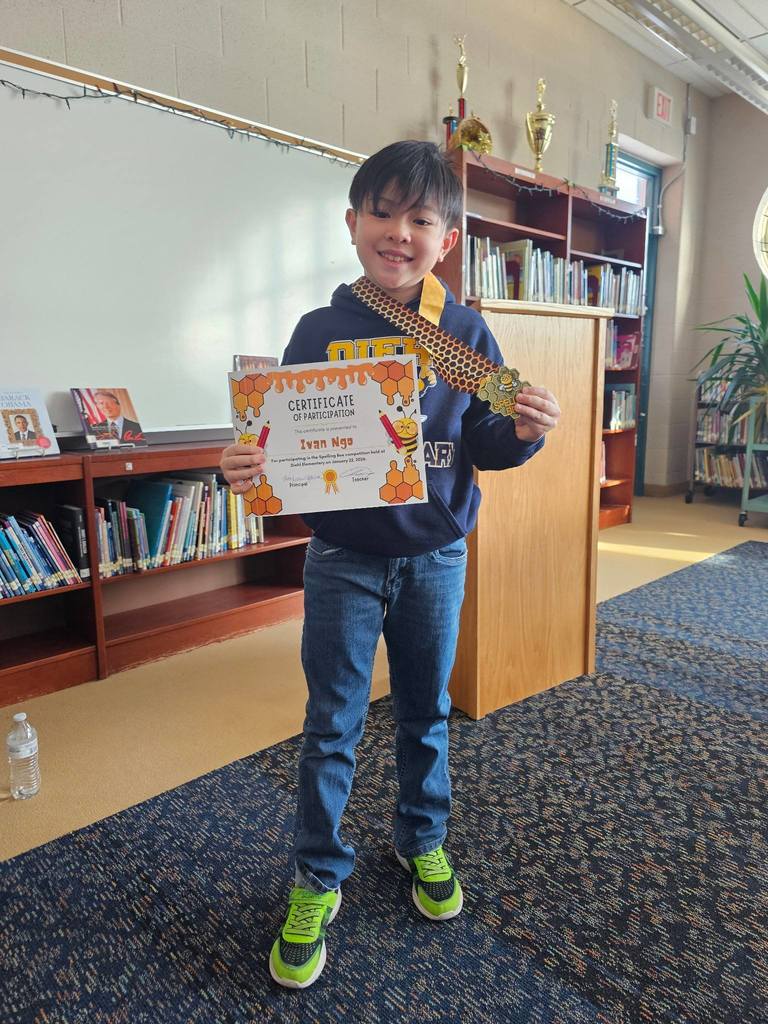Young boy in a classroom holding his certificate and medal.