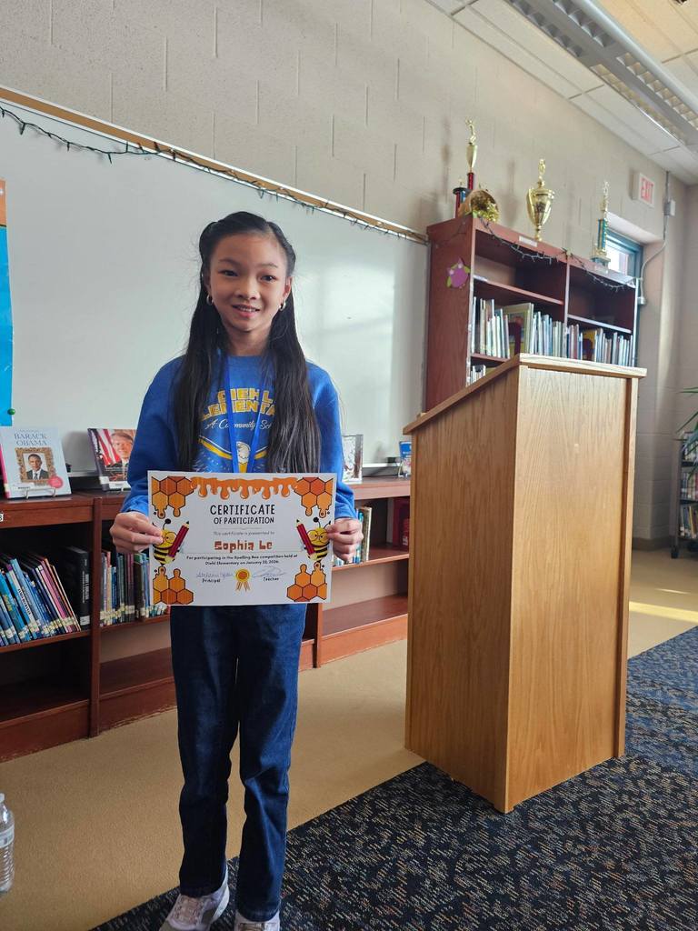 Young girl in a blue shirt holding her certificate.