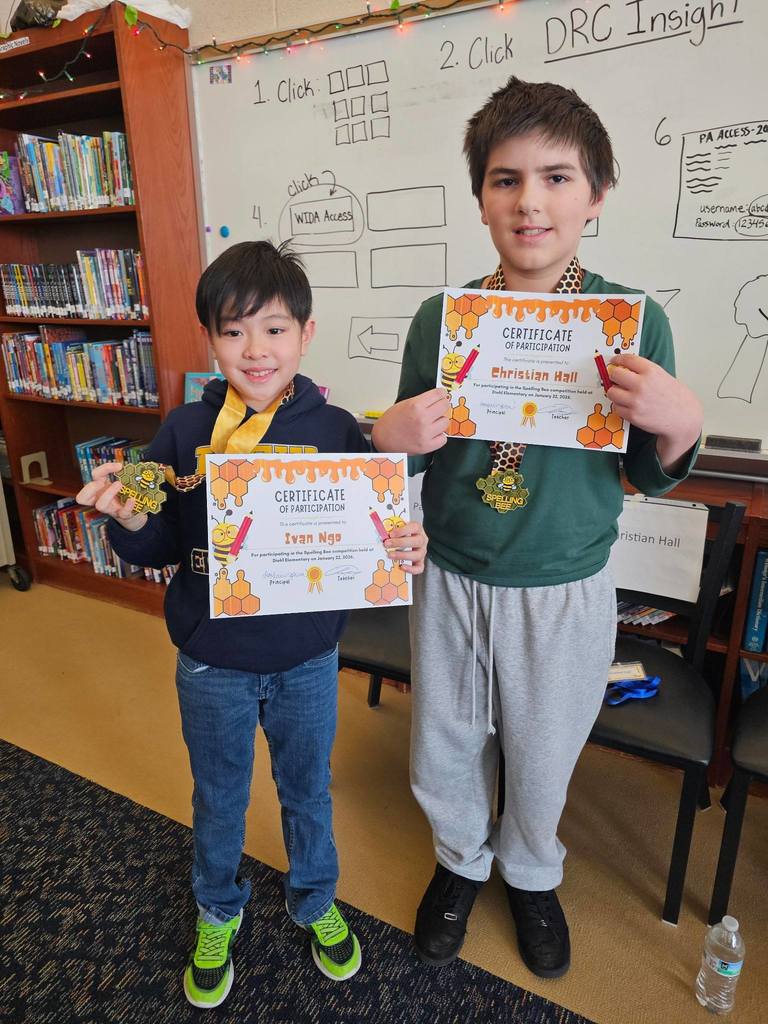 Two young boys holding their certificates and one of them is also holding a medal.
