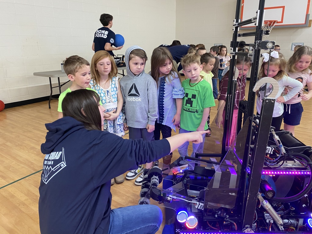 a teen shows a robot to kindergarten students