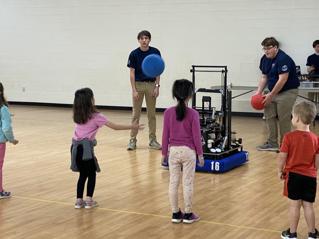 a teen shows a robot to kindergarten students