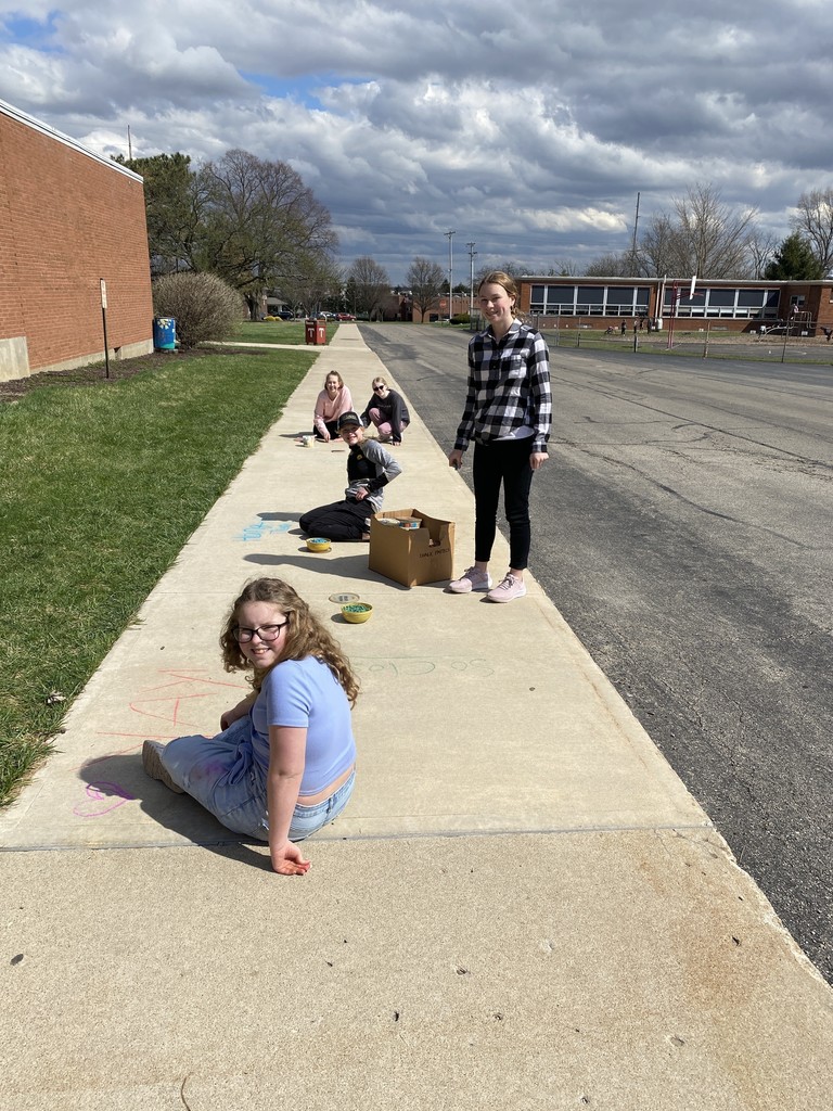 Students are drawing with chalk on the school's walkway.