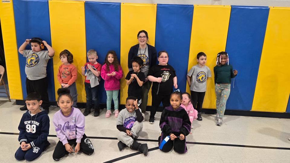 A group of kids with an adult , in front of a blue and yellow wall.