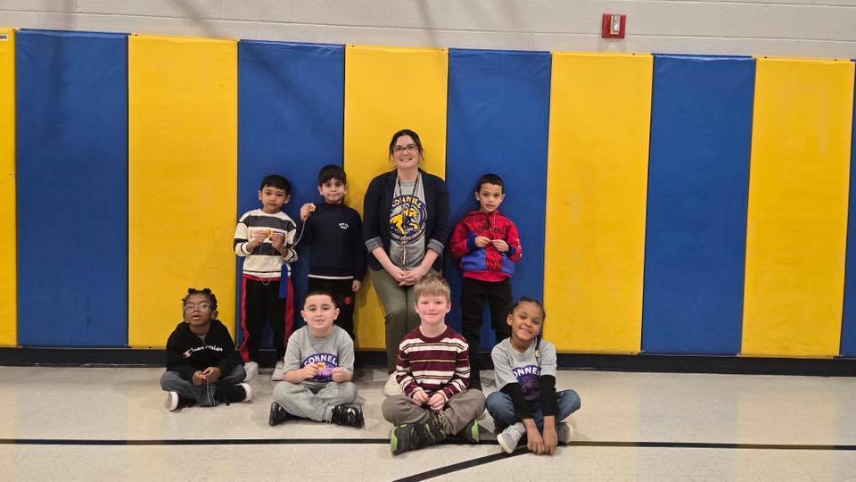 A group of kids with an adult , in front of a blue and yellow wall.