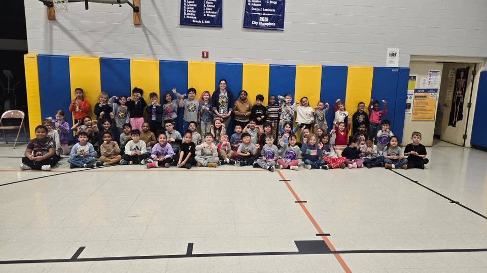 A group of kids with an adult , in front of a blue and yellow wall.