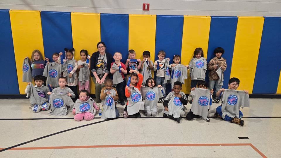A group of kids with an adult , in front of a blue and yellow wall.