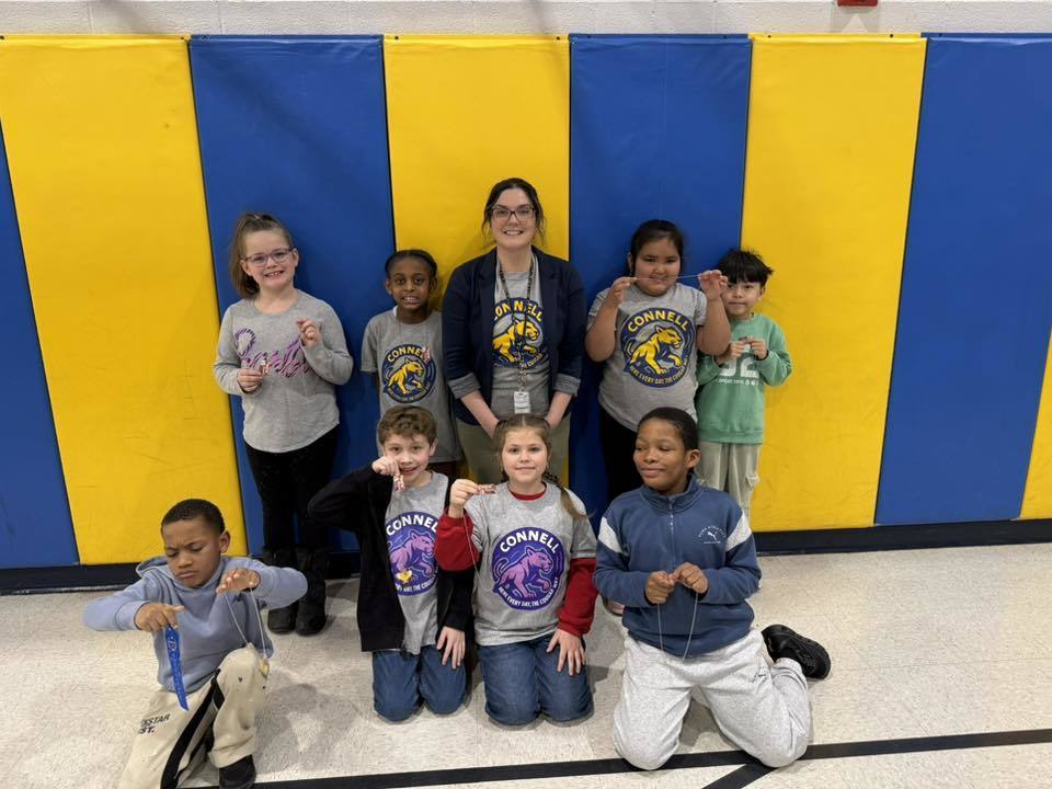 A group of kids with an adult , in front of a blue and yellow wall.