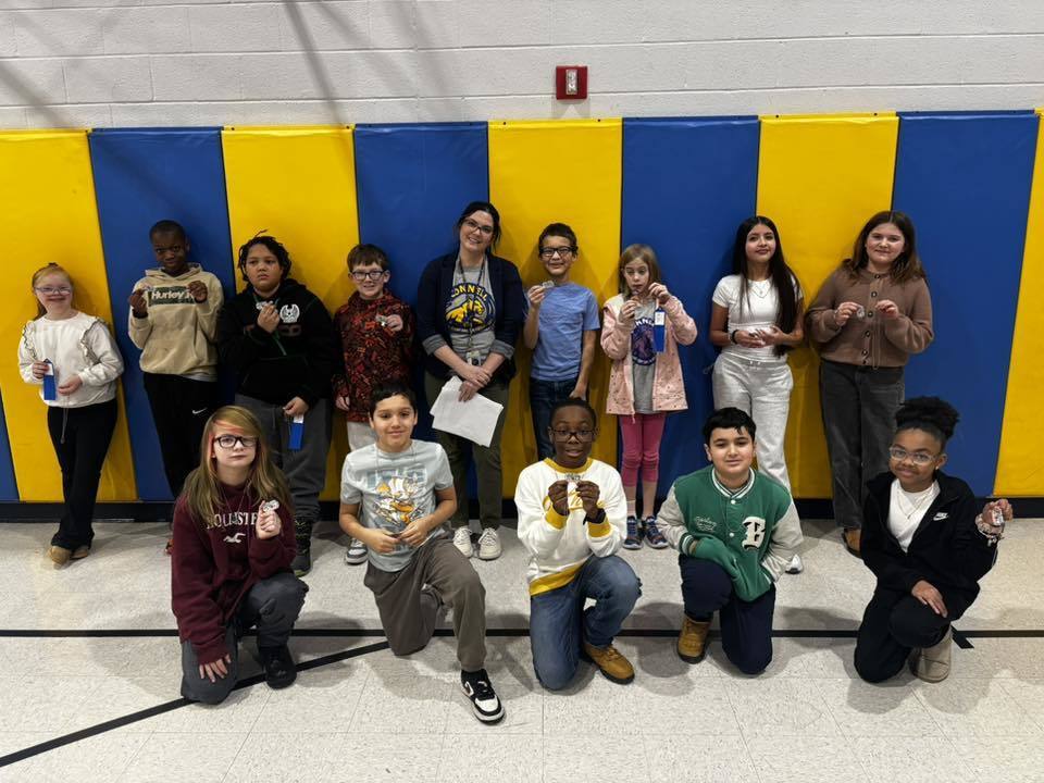 A group of kids with an adult , in front of a blue and yellow wall.