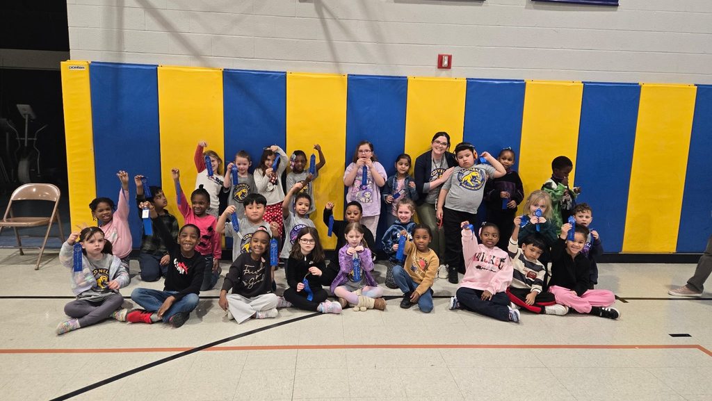 A group of kids with an adult , in front of a blue and yellow wall.