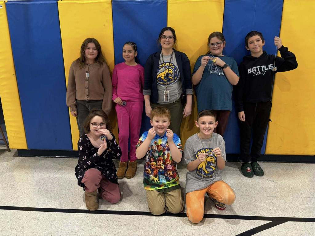 A group of kids with an adult , in front of a blue and yellow wall.