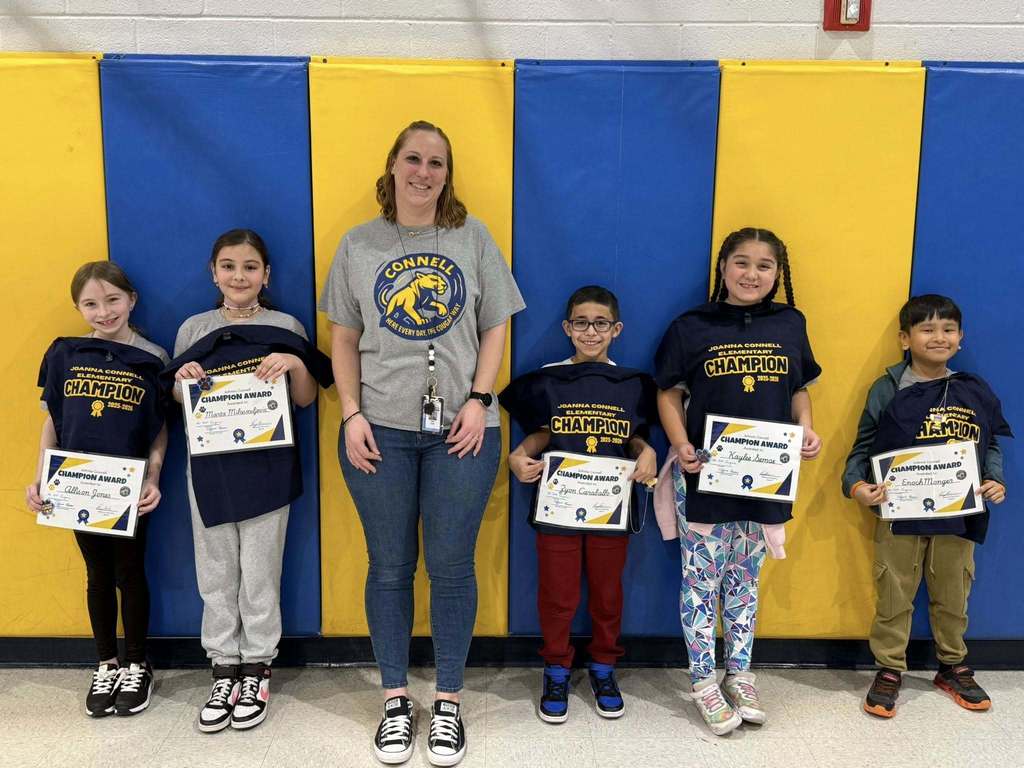A group of kids with an adult , in front of a blue and yellow wall.