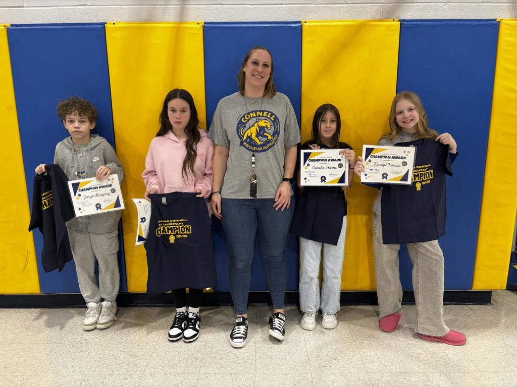 A group of kids with an adult , in front of a blue and yellow wall.