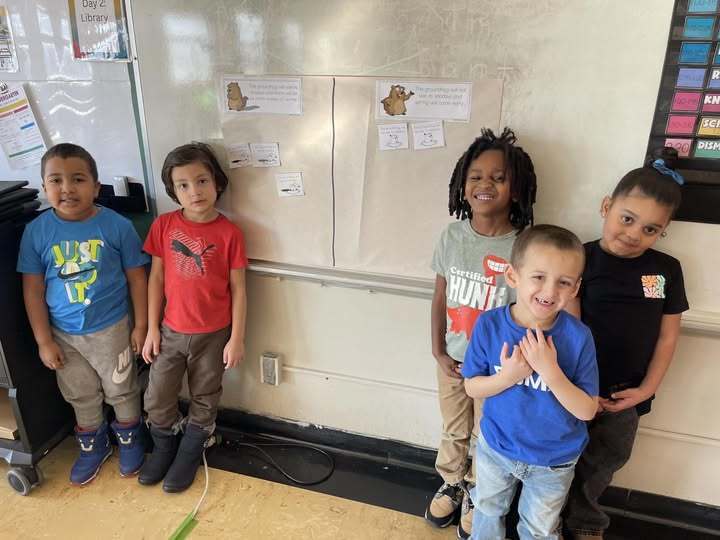 Kids smiling in front of a whiteboard. 