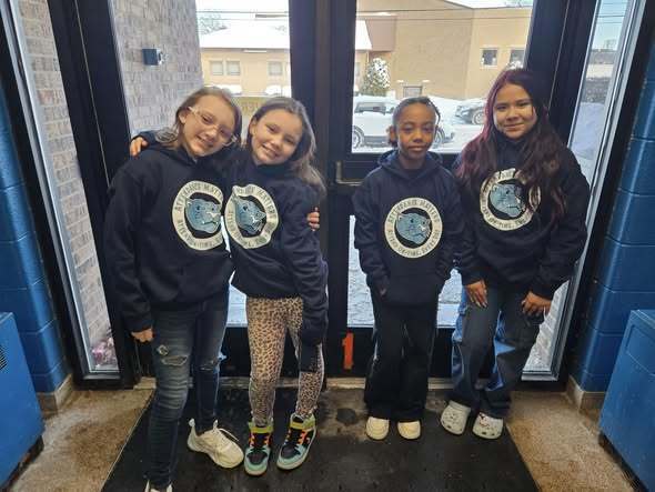 Young girls wearing matching blue hoodies and smiling.
