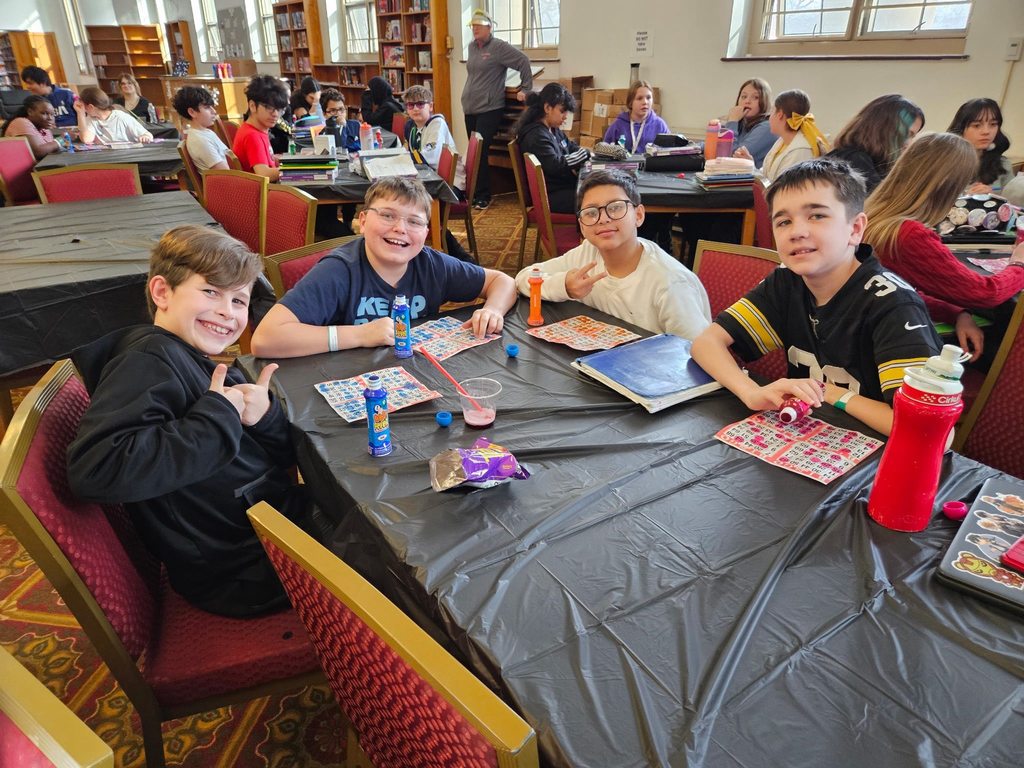 Young boys sitting at a table smiling with bingo cards in front of them.  