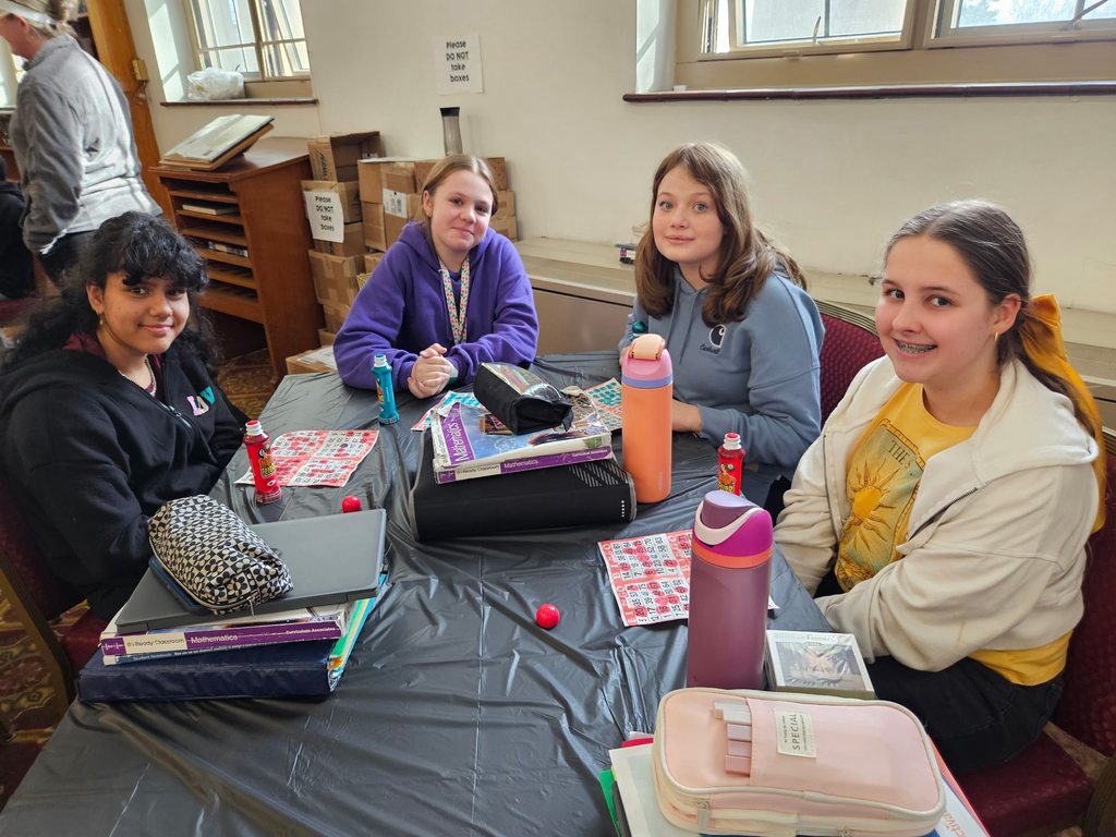 Young girls sitting at a table smiling with bingo cards in front of them.  