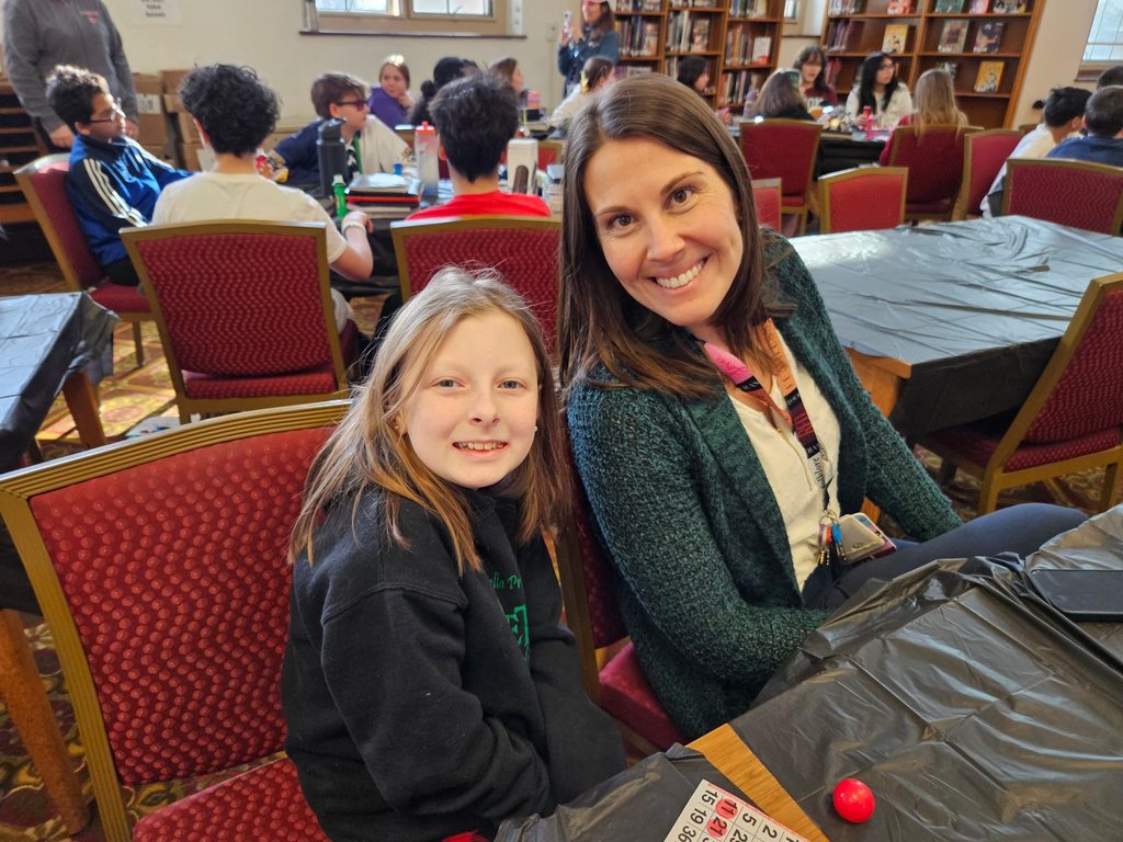 Young girl and female adult sitting at a table and smiling. 