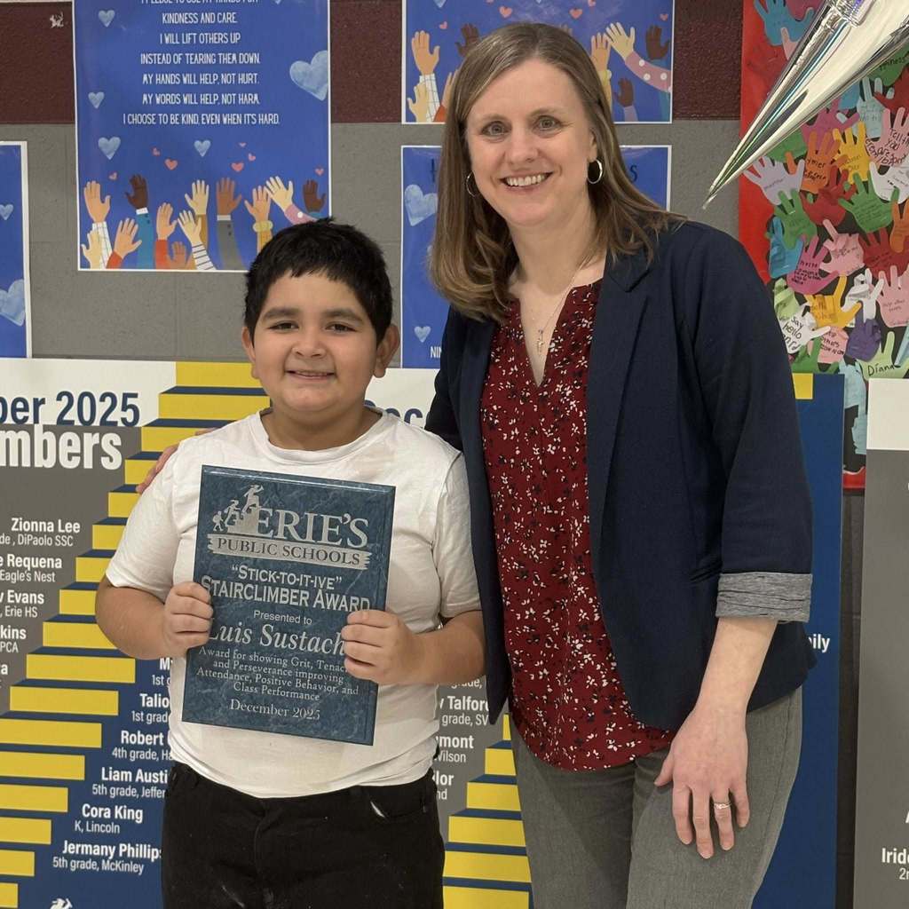 Young boy holding his award and standing next to a female adult. 