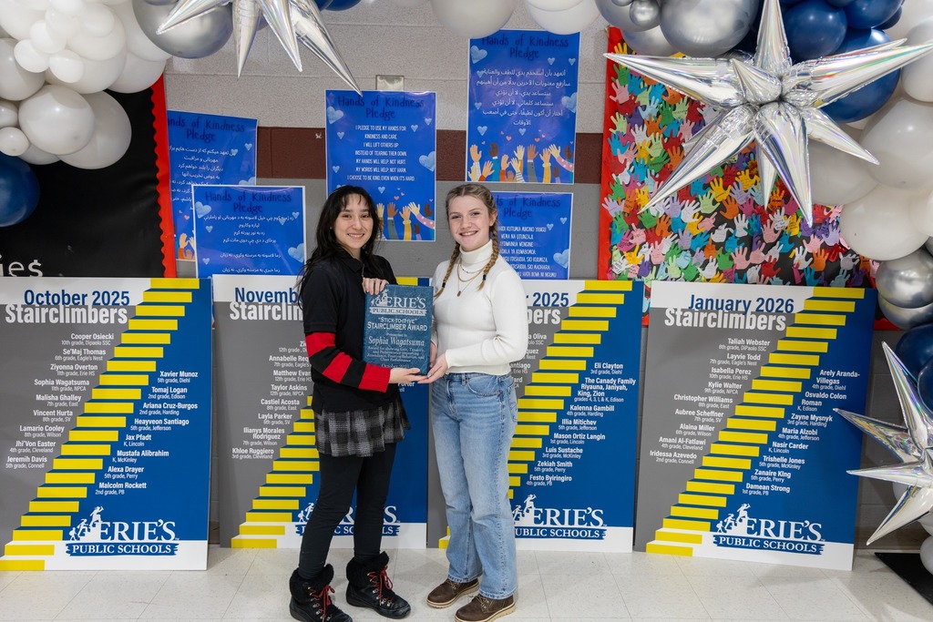 Two young girls smiling and holding an award together. 