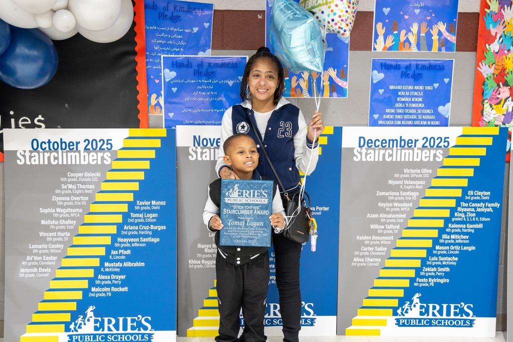 Young boy holding his award while he stands next to a young girl and they are smiling. 