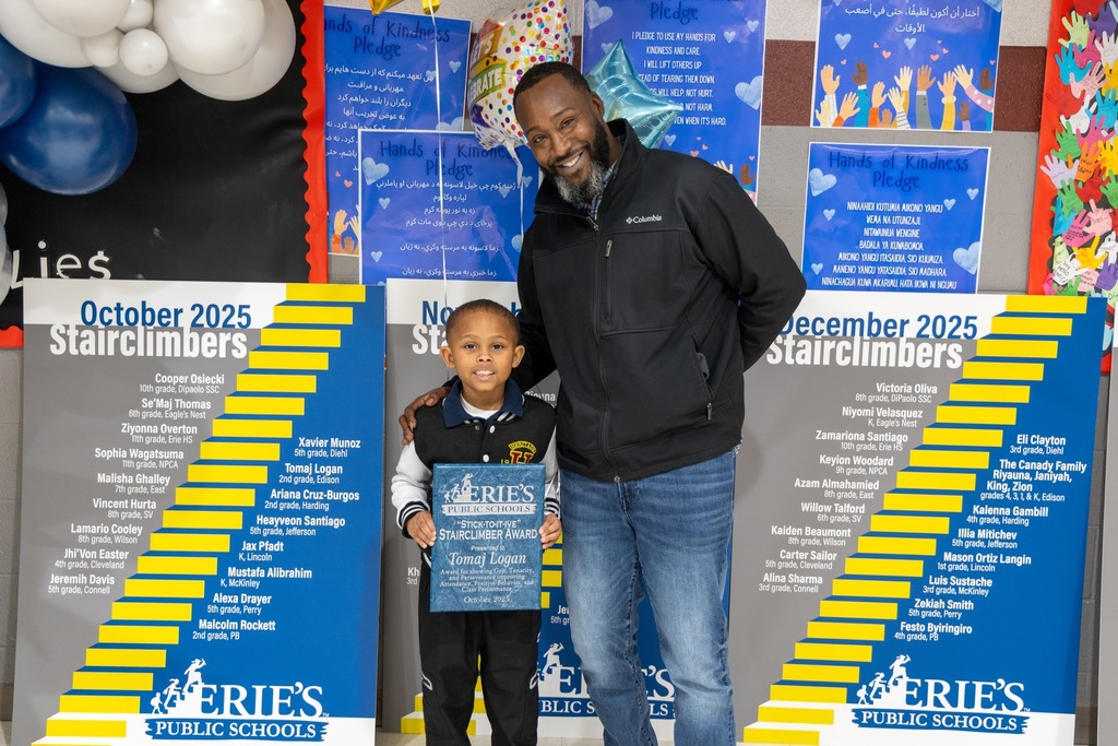 Young boy holding his award while he stands next to a man and they are smiling. 