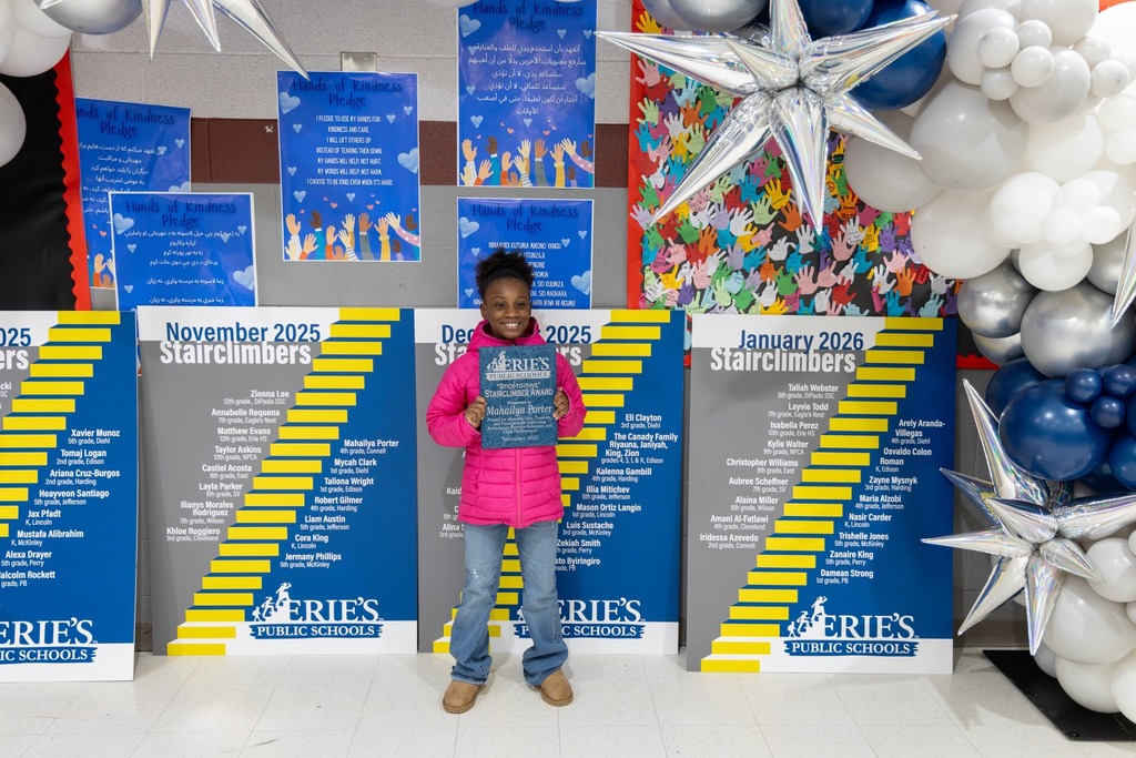 Young girl in a pink jacket smiling and holding her award. 