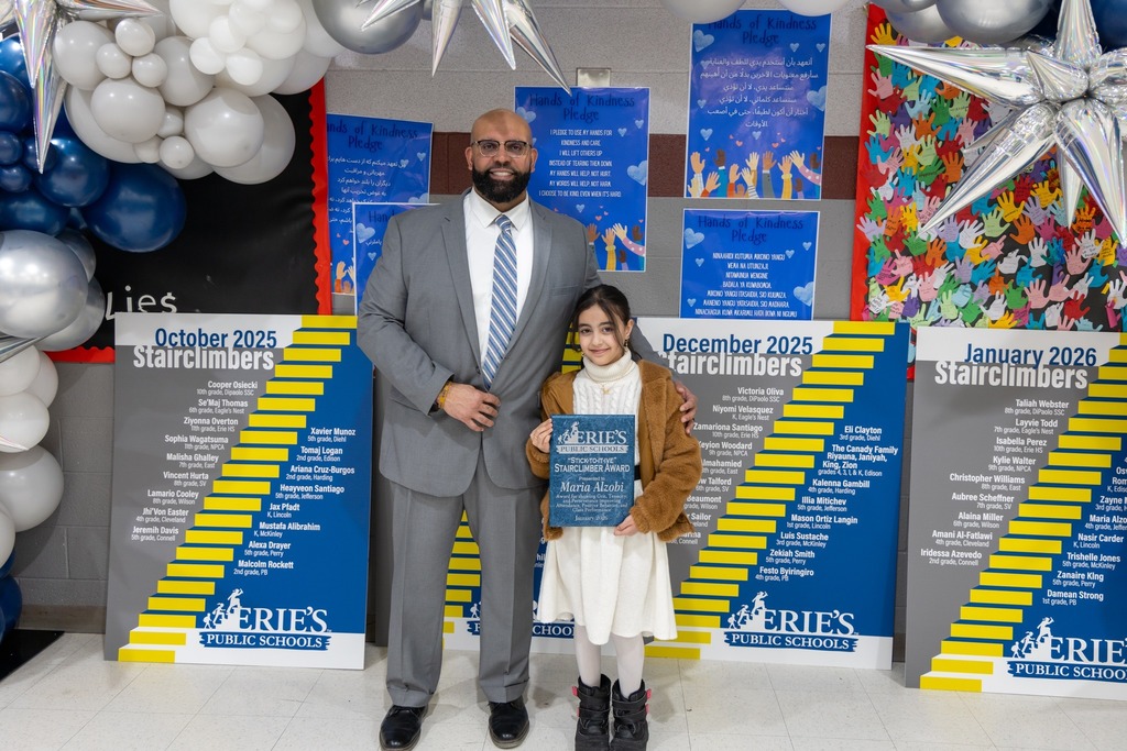 Young girl holding her award while she stands next to a man and they are smiling. 