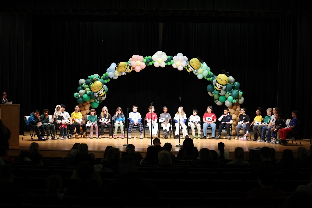 Students sitting on stage with a balloon arch behind them. 