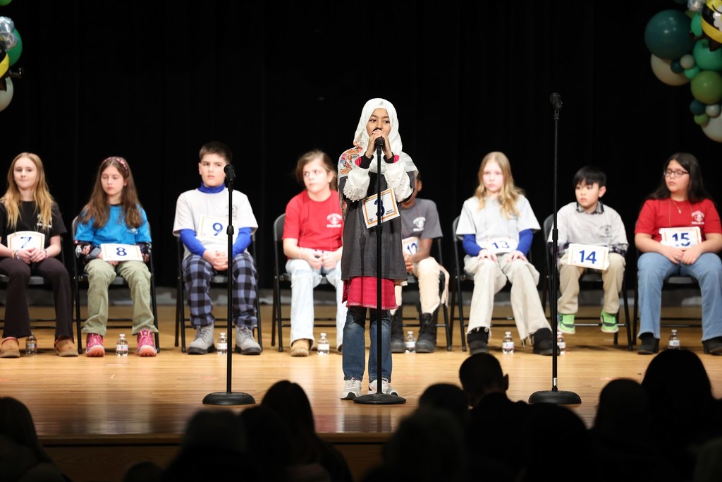 Young girl in a black shirt  speaking into a microphone and standing on stage. 