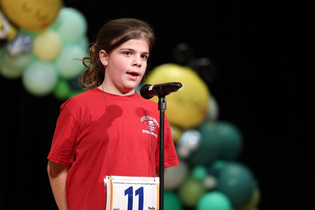 Young girl in a red shirt speaking into a microphone. 